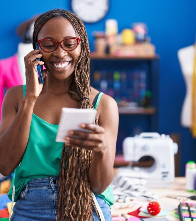 african-american-woman-tailor-talking-smartphone-reading-notebook-atelier_839833-7228